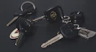 A variety of car key fobs laid out on a wooden workbench with electronic tools nearby