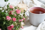 A close-up of a ceramic mug filled with tea resting on a wooden table beside a flickering candle.