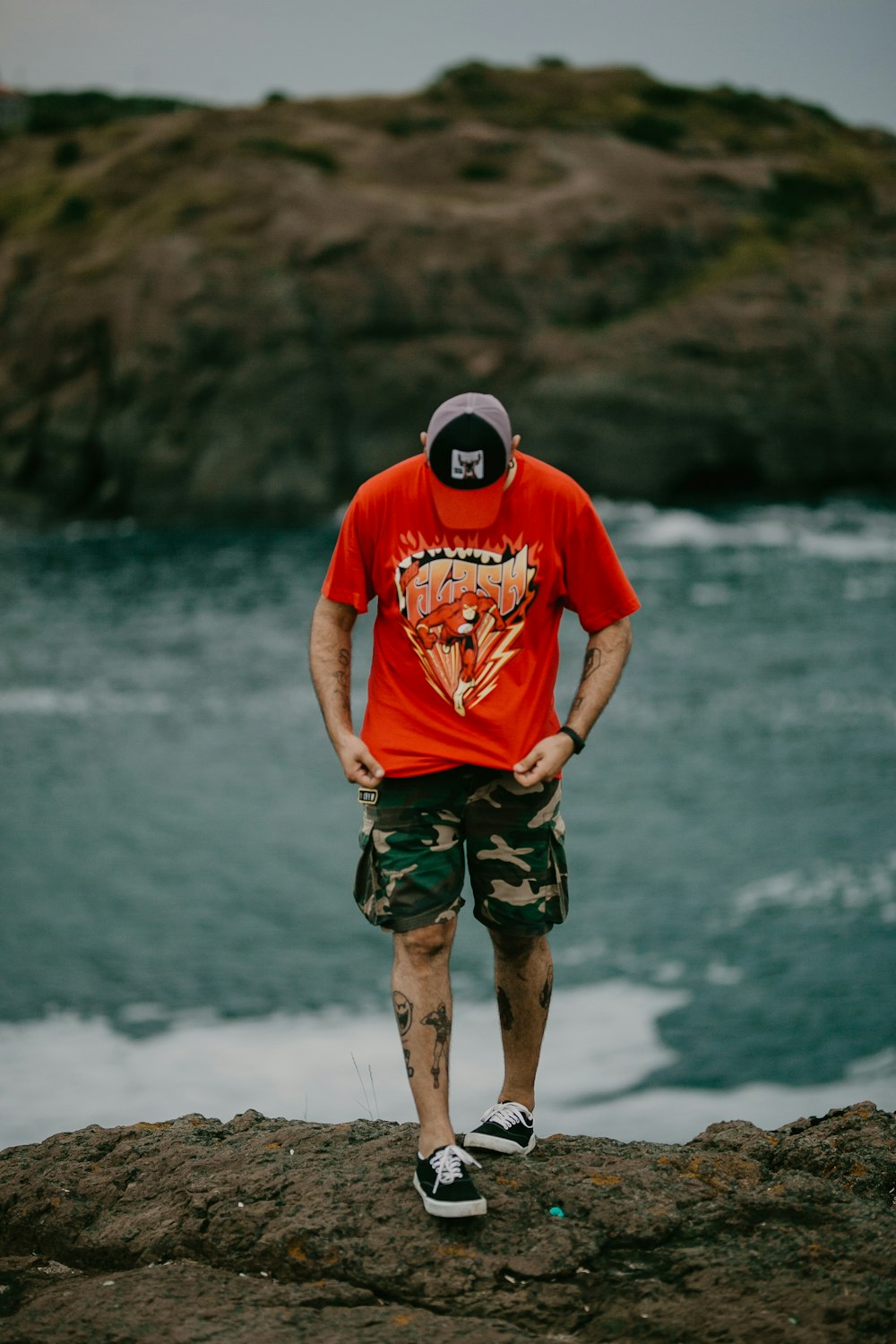 man in red shirt standing on rock near body of water'