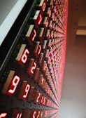 A large grid of glowing red LED numeric displays, arranged in a pattern along a wall. The numbers are illuminated and appear to be counting or representing data in a structured, organized manner.