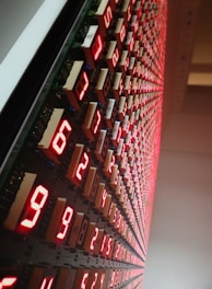 A large grid of glowing red LED numeric displays, arranged in a pattern along a wall. The numbers are illuminated and appear to be counting or representing data in a structured, organized manner.