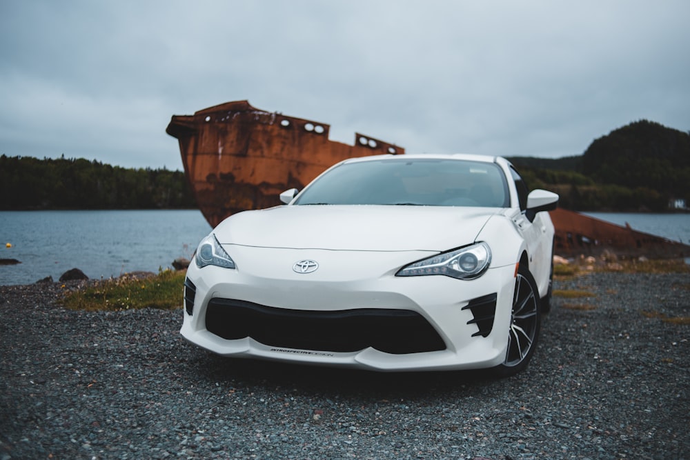 white Toyota car parked in front of wrecked ship on shore