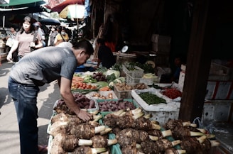 Farmers selecting fresh vegetables at a lively outdoor market.
