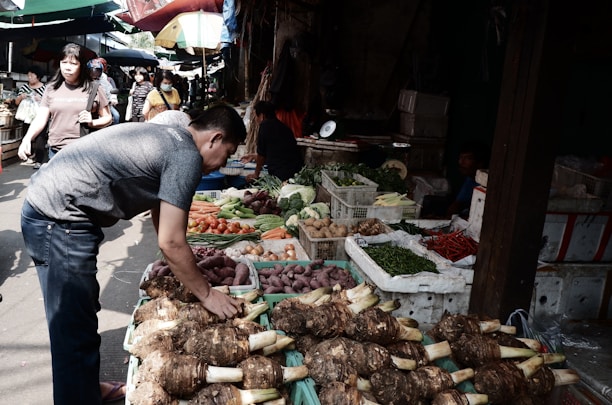 Farmers selecting fresh vegetables at a lively outdoor market.