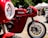 A striking red Ducati motorcycle is prominently displayed, showcasing its sleek design and engineering. The background features a blurred outdoor setting with tents and people, suggesting a bike show or event atmosphere.