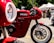 A striking red Ducati motorcycle is prominently displayed, showcasing its sleek design and engineering. The background features a blurred outdoor setting with tents and people, suggesting a bike show or event atmosphere.