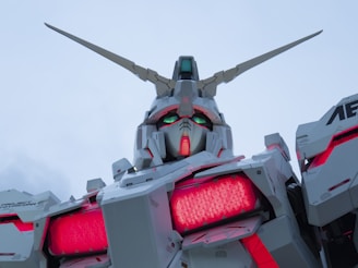A large, detailed robot with angular features and horns on its head. The robot has a shiny white and gray exterior with red and green lights illuminating from its eyes and chest area. The background is a cloudy sky, giving an impression of grandeur and presence.