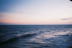 Calm ocean waves under a pastel blue sky at sunset.