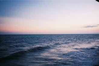 Calm ocean waves under a pastel blue sky at sunset.