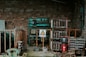 An industrial setting with exposed electrical equipment housed against a brick wall. The equipment consists of various transformers, circuit breakers, and wiring, enclosed within metal racks. A warning sign in a triangle is prominently displayed, indicating high voltage, and is written in Chinese. The scene has an abandoned and slightly rustic feel, with some rust and overgrown plants visible.