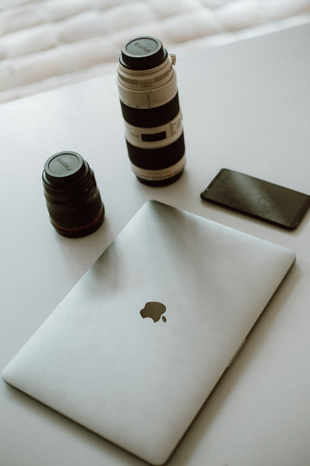 silver MacBook and white and black DSLR camera lens on gray surface