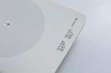 A minimalist design artifact featuring a circular pattern of blue dots on a white background. Near the bottom right corner, there is text printed in a monochrome typewriter-style font. The paper has slightly curved corners and is set against a light grey surface.