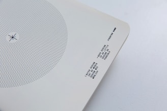 A minimalist design artifact featuring a circular pattern of blue dots on a white background. Near the bottom right corner, there is text printed in a monochrome typewriter-style font. The paper has slightly curved corners and is set against a light grey surface.