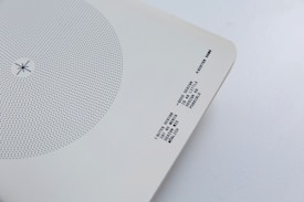 A minimalist design artifact featuring a circular pattern of blue dots on a white background. Near the bottom right corner, there is text printed in a monochrome typewriter-style font. The paper has slightly curved corners and is set against a light grey surface.
