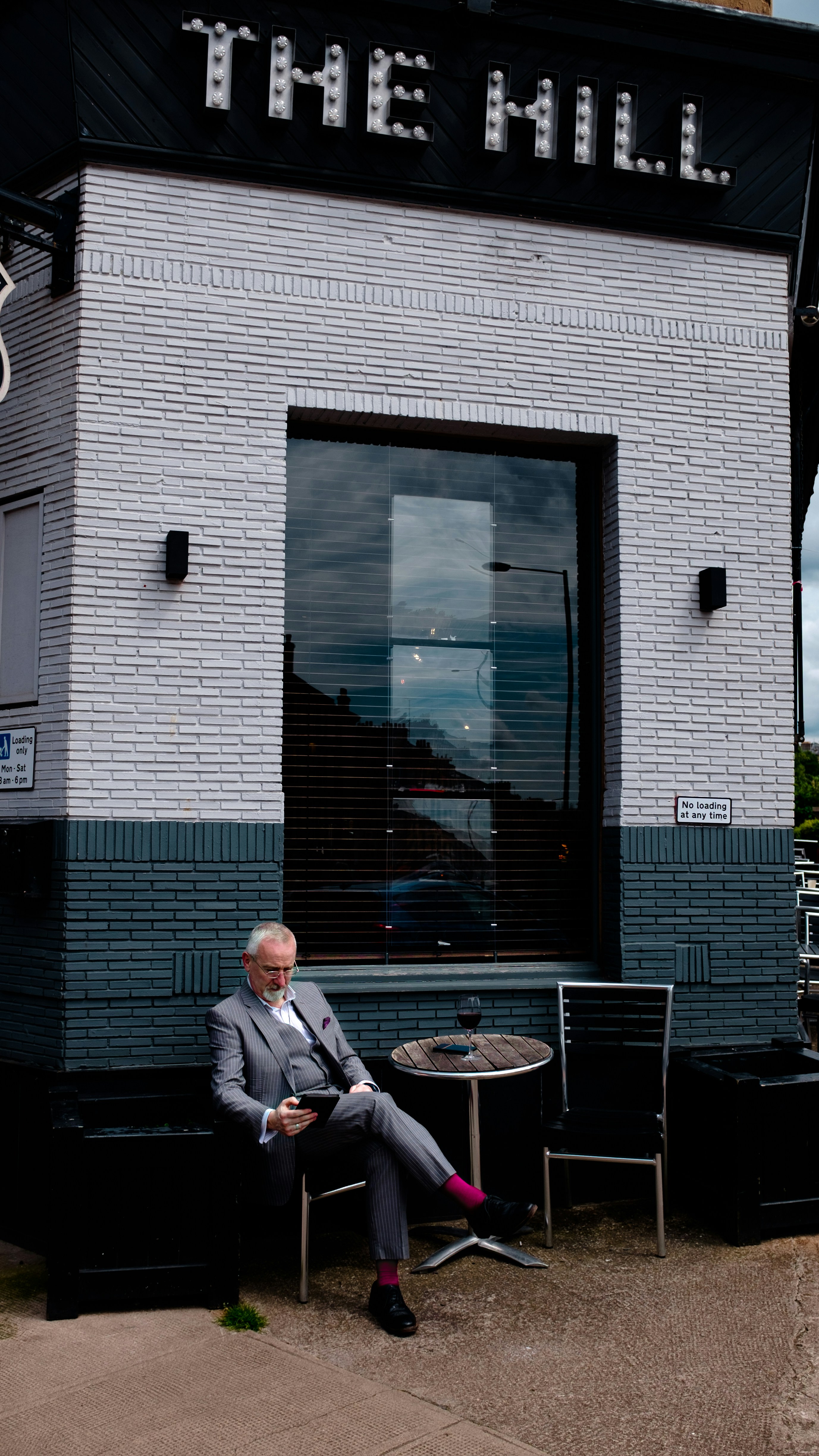 man in grey suit sitting on chair beside table in front of The Hill building