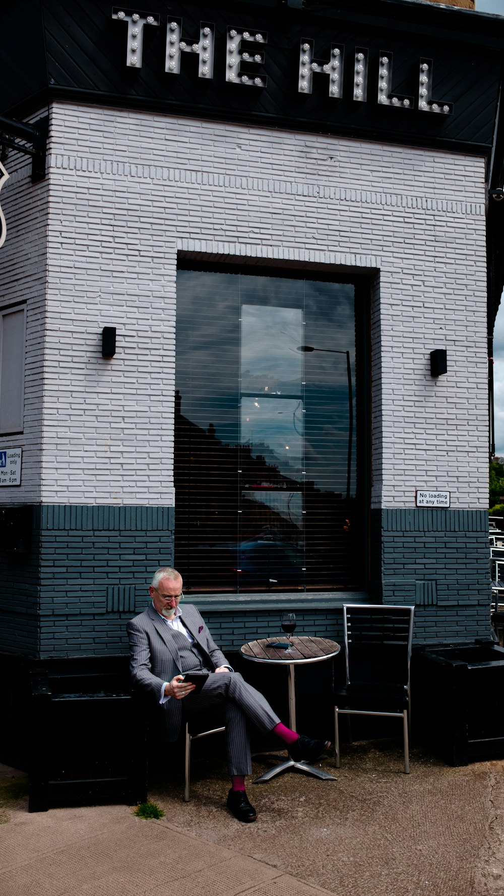 man in grey suit sitting on chair beside table in front of The Hill building