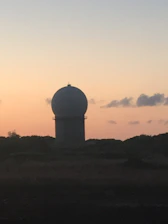 Close-up of advanced radar and optical sensors scanning the sky at dusk.