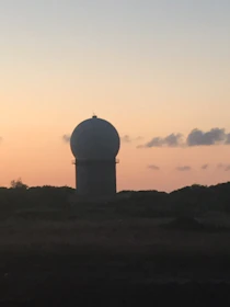 Close-up of advanced radar and optical sensors scanning the sky at dusk.