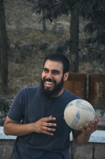 A teenager holding a green and white soccer ball with a joyful smile