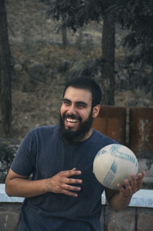 Happy customer holding a soccer ball outdoors with a bright smile, green field in the background.
