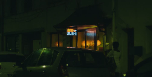 Dimly lit sushi bar with neon signs casting vibrant colors on the chefs at work.
