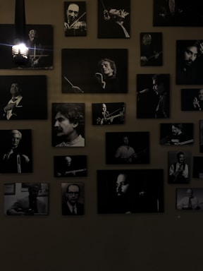 A collection of black and white portraits of musicians is arranged on the wall. Each framed photograph captures a musician either in the midst of playing an instrument or posing with one. The lights add a dramatic shadow, emphasizing the black and white contrasts. The overall atmosphere is artistic and vintage.