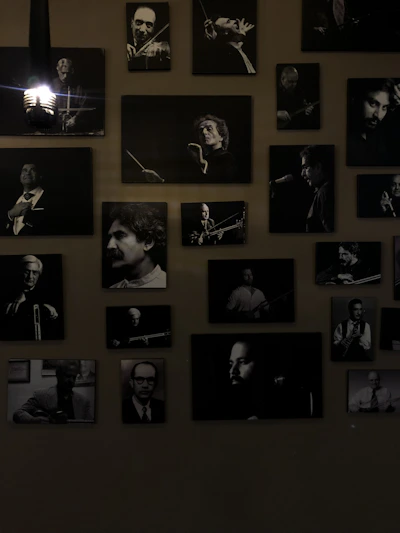 A collection of black and white portraits of musicians is arranged on the wall. Each framed photograph captures a musician either in the midst of playing an instrument or posing with one. The lights add a dramatic shadow, emphasizing the black and white contrasts. The overall atmosphere is artistic and vintage.