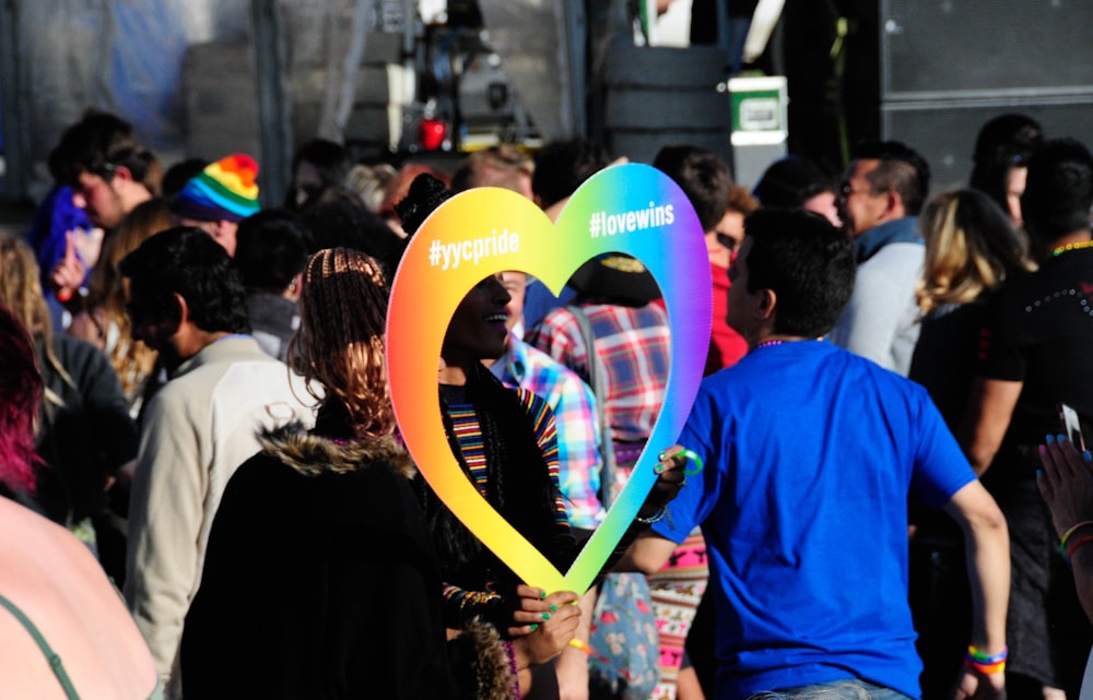 person holding multicolored heart frame across people