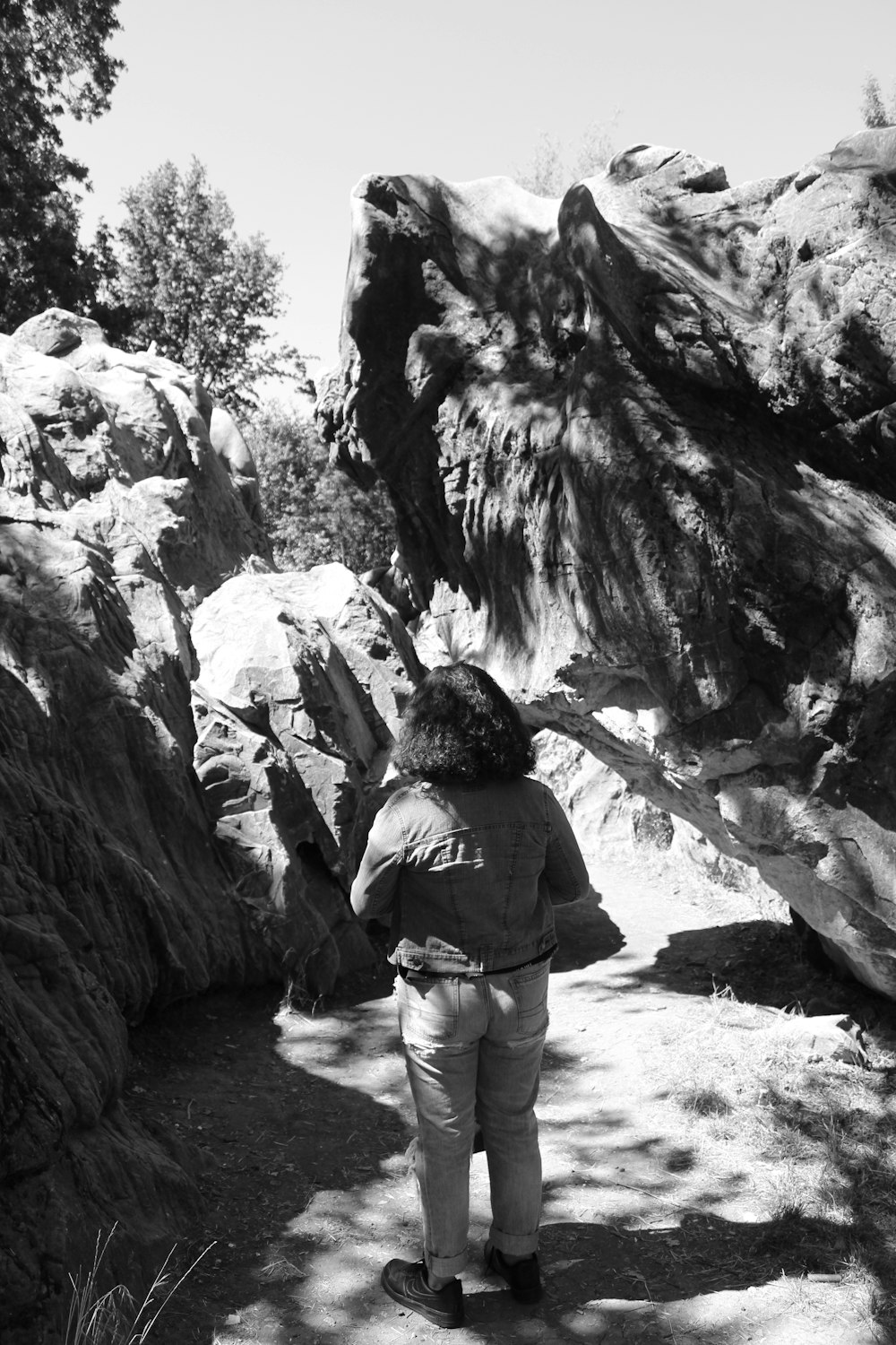 grayscale photography of woman standing near rock formation