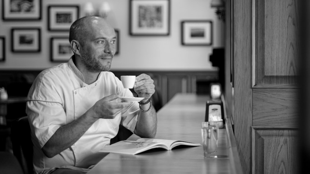 grayscale photo of man holding cup and saucer