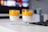 Two glasses of chia pudding topped with a bright orange mango puree are placed on a white table. The background includes a blurred television screen and a small potted plant.