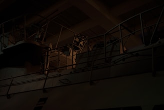A dark, industrial setting featuring metal railings and possibly machinery with dim lighting creating shadows and highlights.