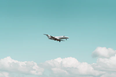 A cheerful cartoon cat pilot wearing aviator goggles, flying a small airplane through fluffy clouds.