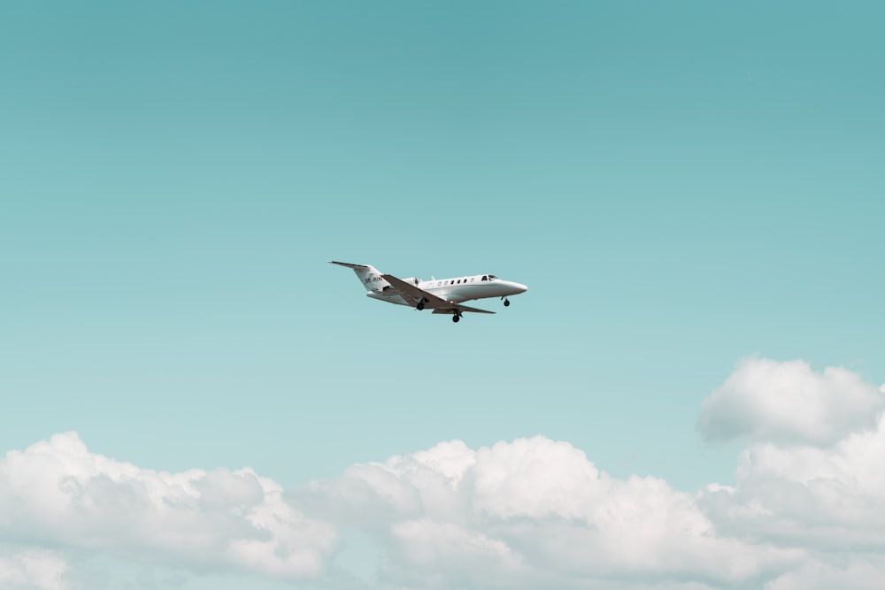 white airplane flying under Cumulus clouds