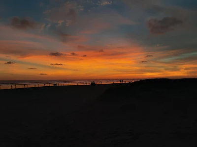 A vibrant sunset over a serene beach with travelers enjoying the view.