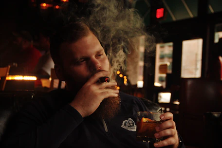 Charles Trent studying basketball stats with a cigar in hand and bourbon glass nearby.