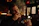 A smiling middle-aged man enjoying a glass of whisky in a cozy, wood-paneled tasting room.
