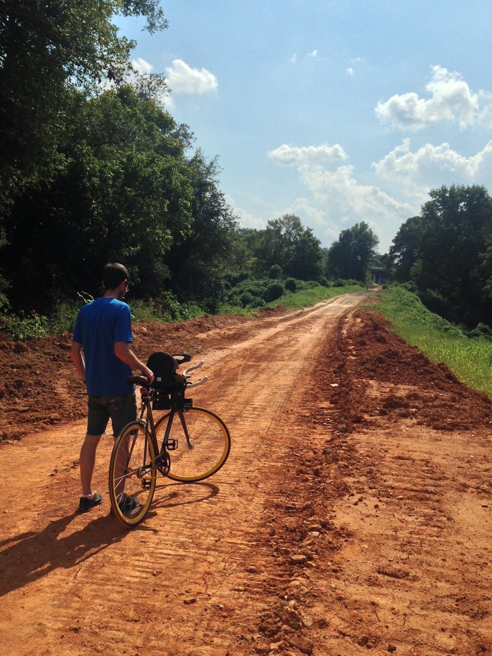 man standing and holding road bike on dirt road near trees