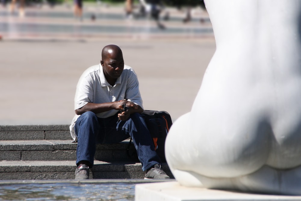 Fotografia de foco seletivo do homem sentado ao lado da fonte de água com estátua