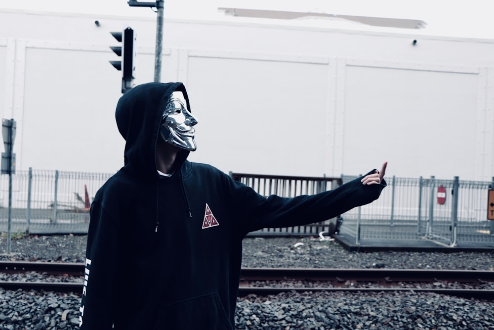 person wearing guy fawkes mask standing near train railway