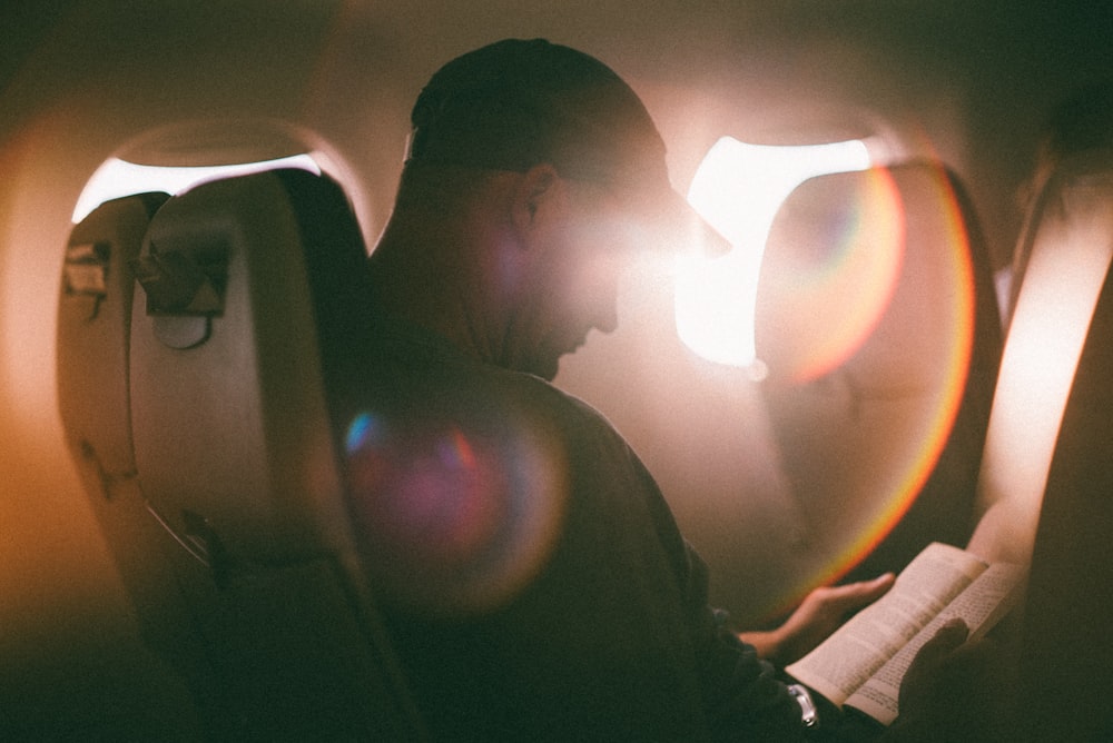 man sitting and reading book inside airplane