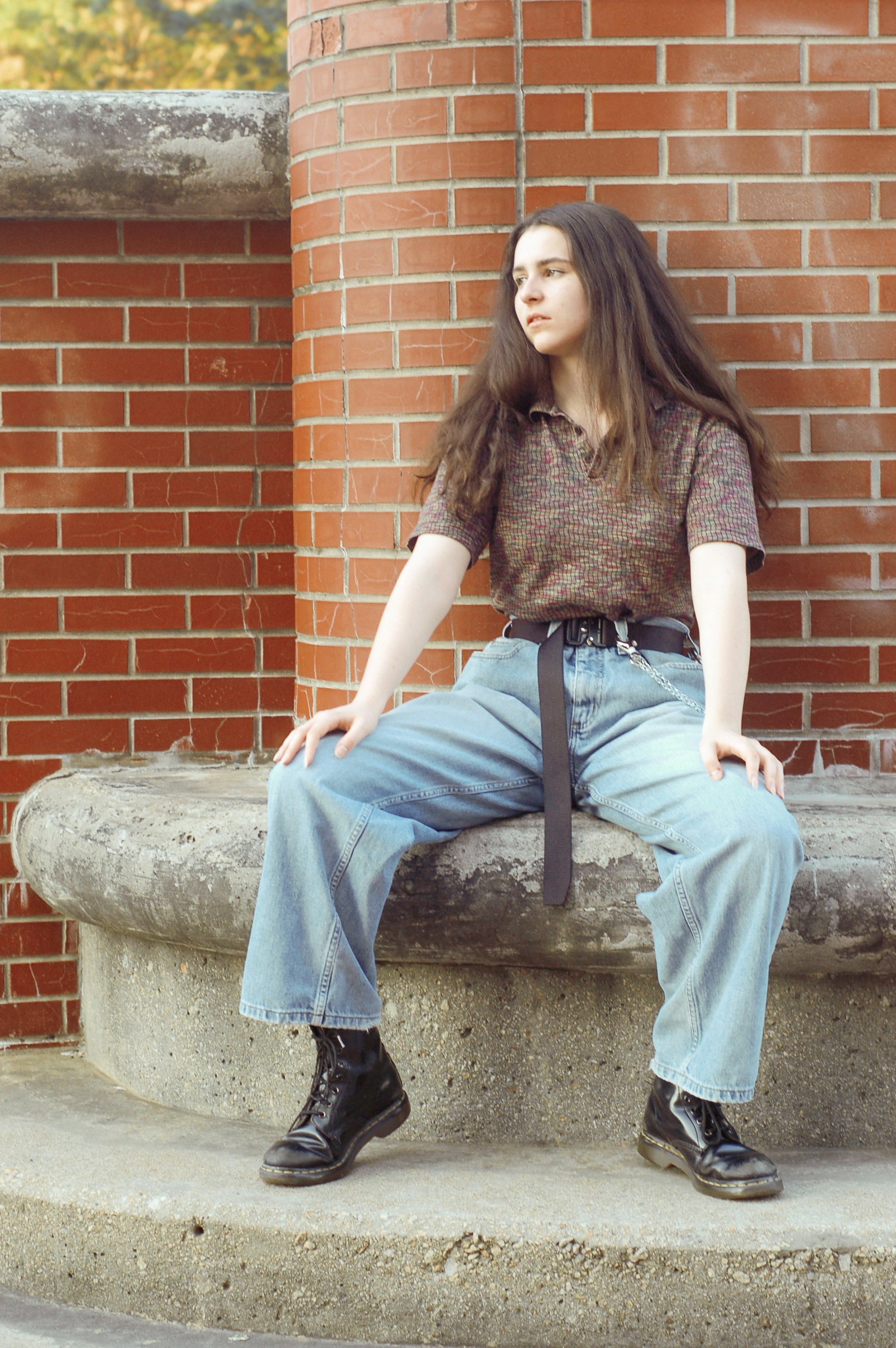 Woman in loose, light-wash wide-leg jeans sitting on a stone ledge against a brick wall