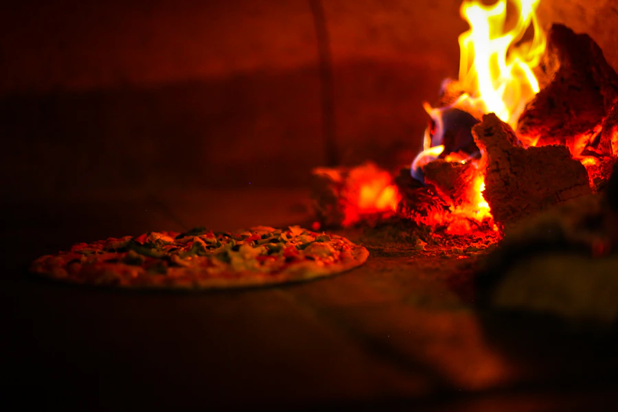A pizza baking deep inside a wood-fired oven beside a stack of burning logs