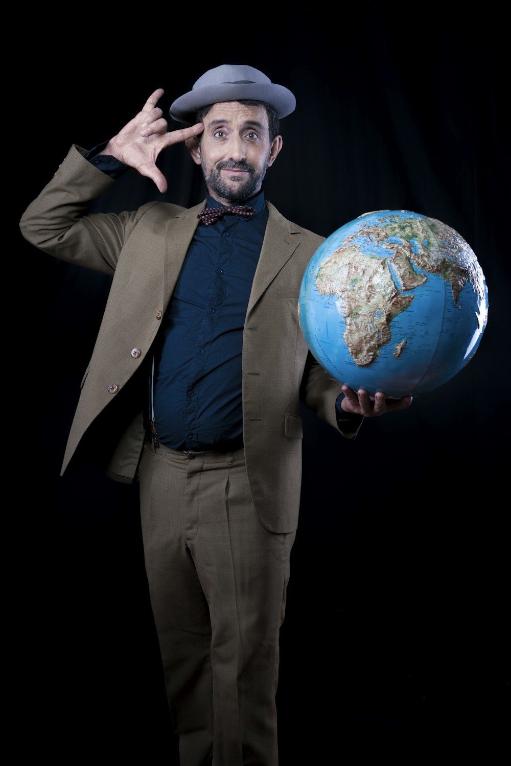 man in brown suit jacket and dress pants holding planet earth toy