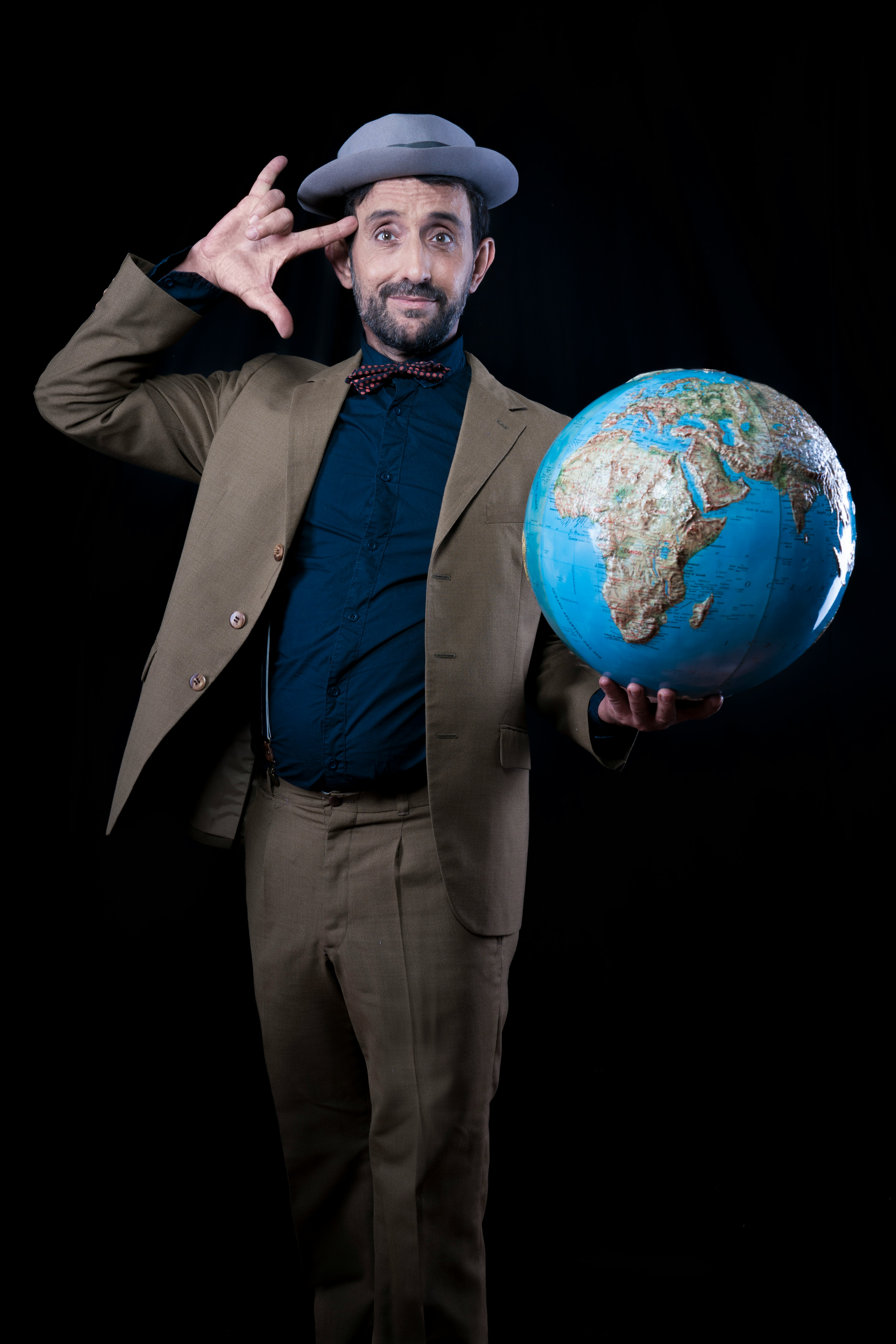 man in brown suit jacket and dress pants holding planet earth toy