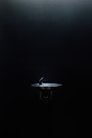 A drinking fountain is centered in an otherwise dimly lit environment, with light highlighting its metallic surface against the dark background.