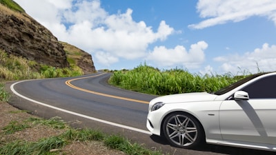 Sleek car parked by a scenic coastal road with mountains.