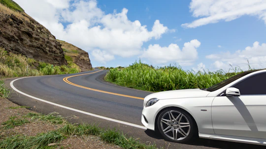 A sleek rental car parked beside a scenic mountain road under a clear blue sky.