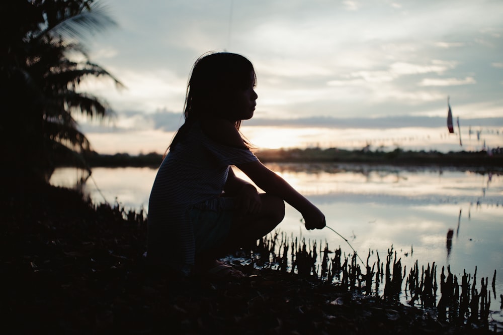 silhouette of girl squatting near body of water