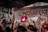 A lively music concert with a band performing on stage. The crowd is engaged, raising their hands in enthusiasm, and the backdrop reads 'MOSAFEST' indicating a festival setting.